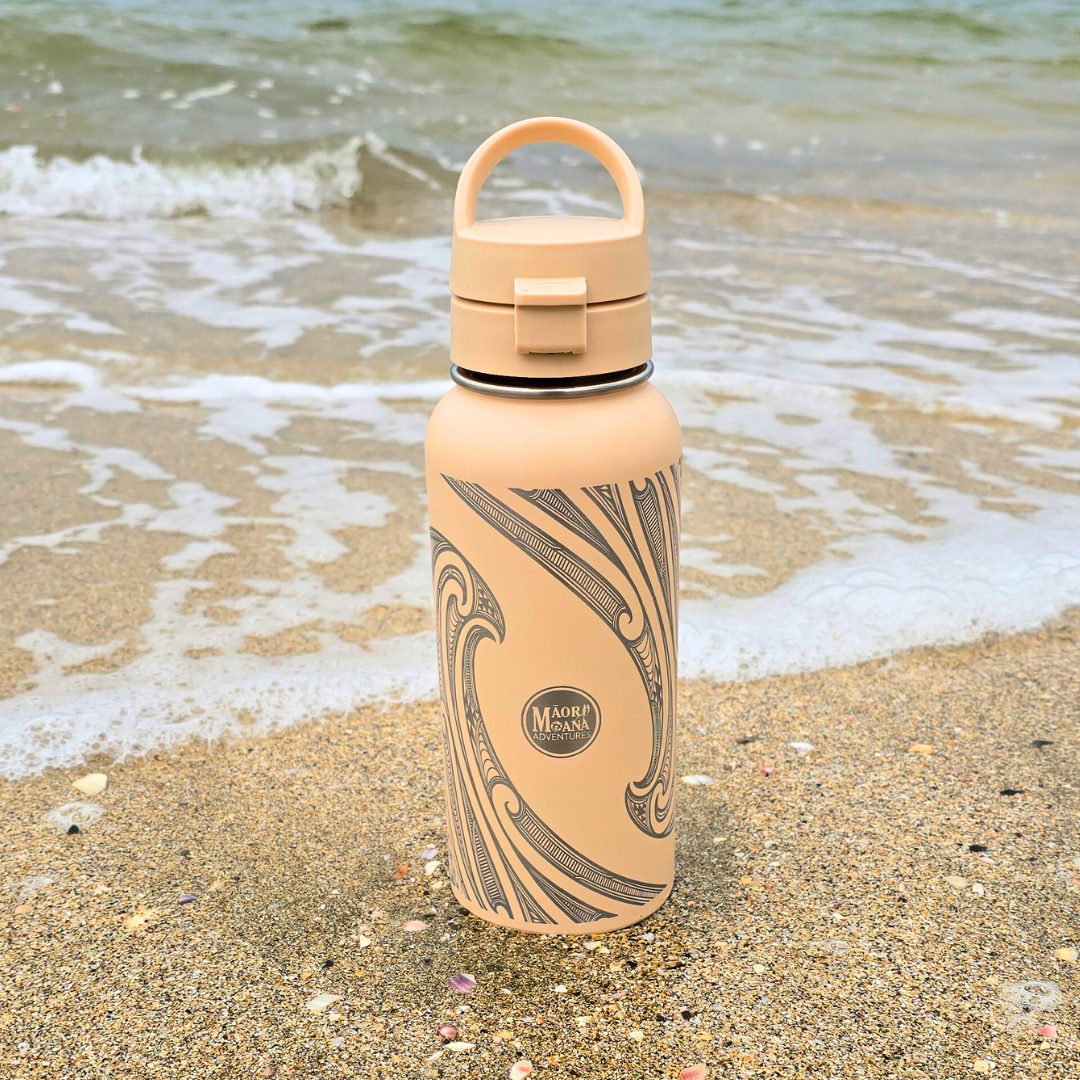 Beige water bottle with maori patterns on a sandy beach
