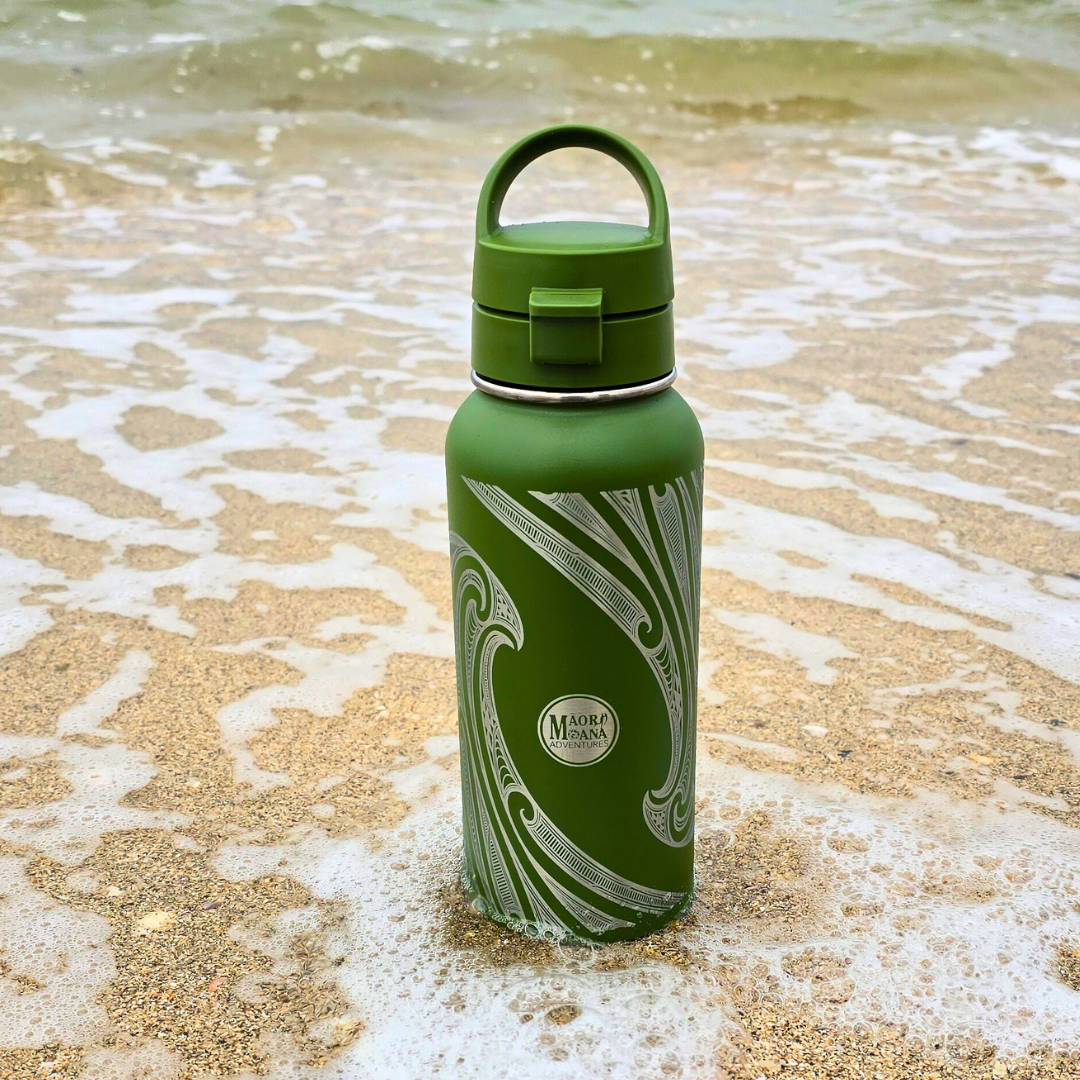 Green water bottle with a decorative pattern on a sandy beach