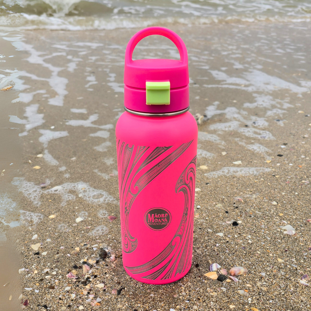 Pink water bottle with a green cap on a sandy beach