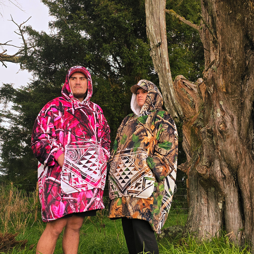 Two people wearing camo ponchos standing in a forested area.