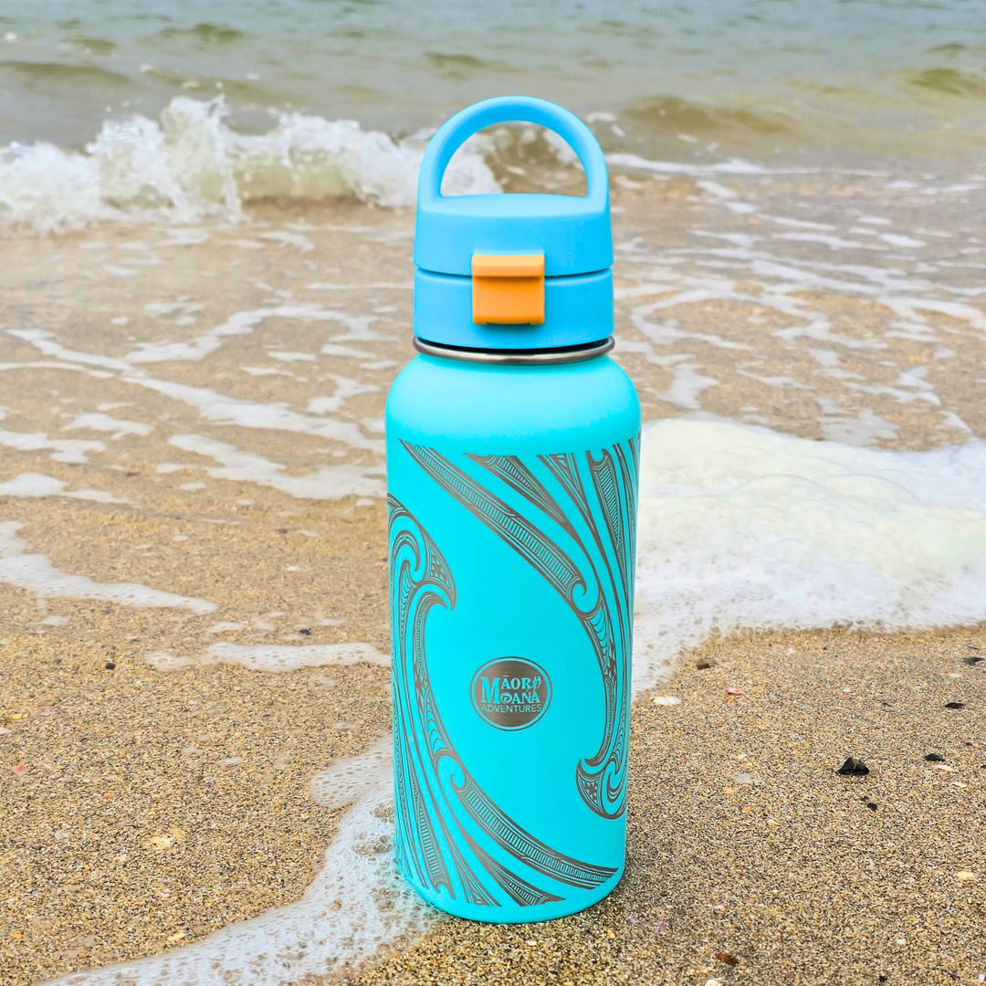 Turquoise water bottle with a handle on a sandy beach with ocean waves.